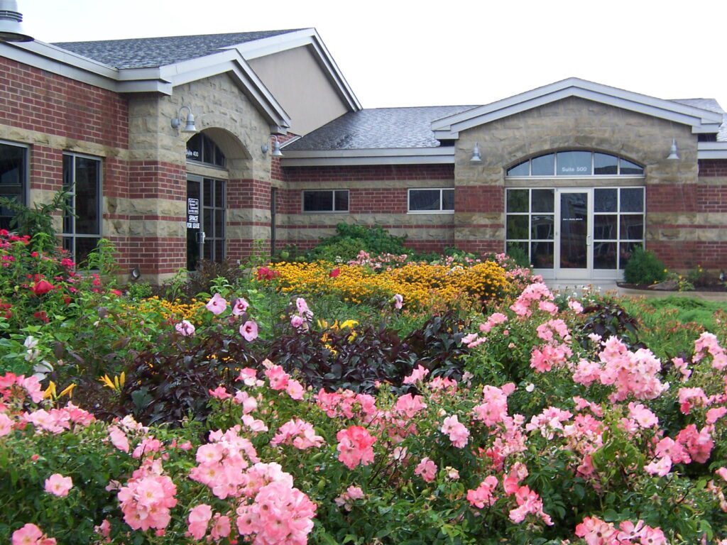 A wide shot of a commercial property's main entrance, featuring abundant and colorful perennial and annual flower beds.